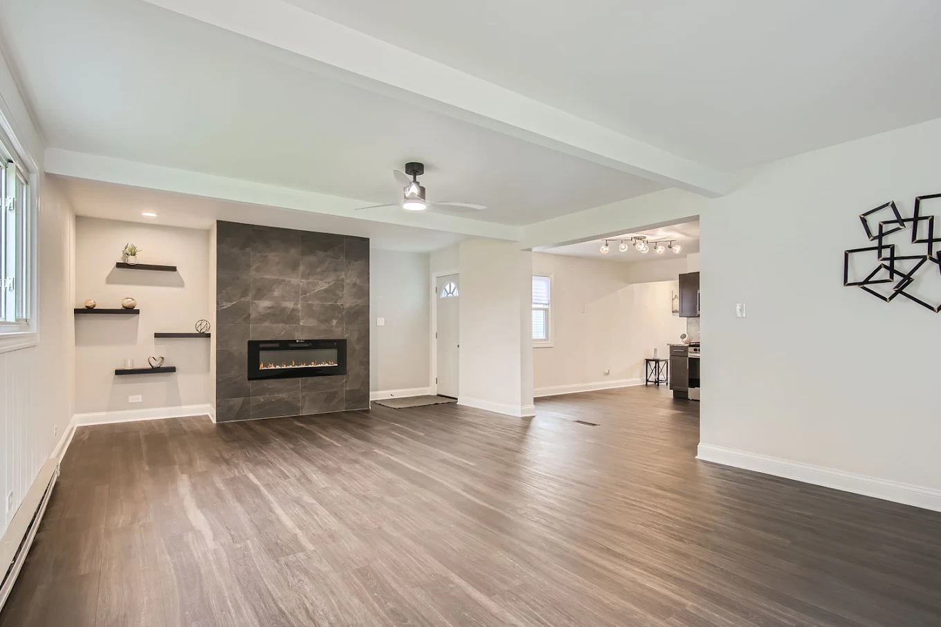 Open Kitchen & Living Room after photo: Living room with tile fireplace wall, floating shelves, and open view to the kitchen
