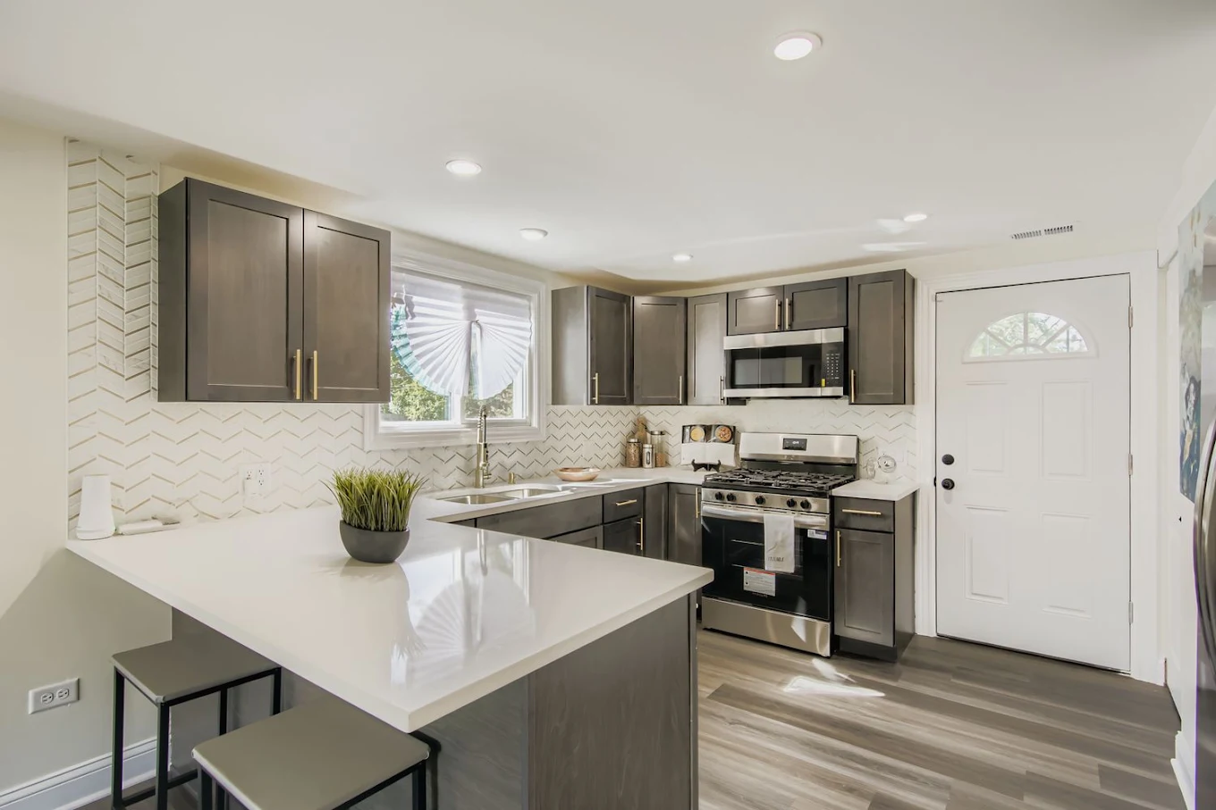 Chevron Backsplash & Quartz Peninsula after photo: Gray shaker cabinets, quartz peninsula, and chevron tile backsplash