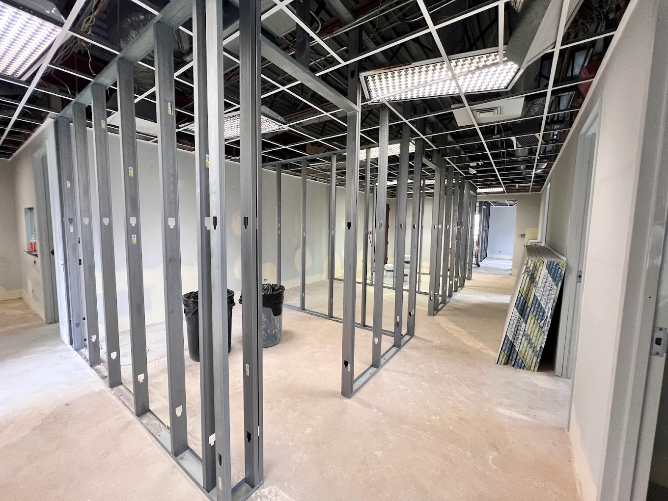 Commercial office build-out during framing, with metal studs, a swept concrete floor, and neatly stacked drywall
