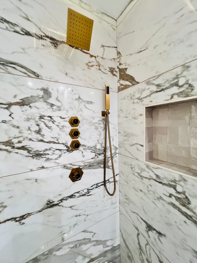 Marble & Gold Primary Bath after photo: Shower valves, hand shower, and tiled niche